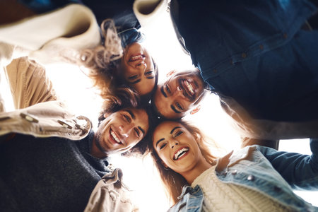 Low angle portrait of a group of young friends huddled together while looking down at the camera...