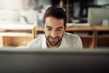 All part of the process of success. a handsome young businessman working late on a computer in an...