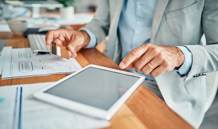 Never far from his workstation. Closeup shot of an unrecognizable businessman using a digital tablet while holding a credit card in an office.の写真素材