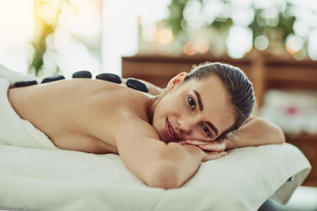 Nothing makes me relax like a hot stone massage. Portrait of an attractive young woman getting a hot stone massage at a beauty spa.の写真素材