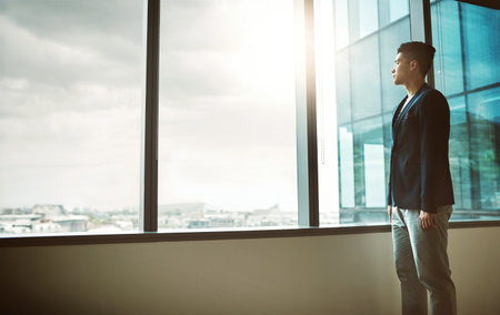 He came here to conquer. a young businessman looking thoughtfully out of an office window.の写真素材