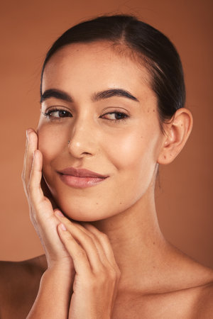 Skincare, beauty and face of Latina woman with smile, healthy and natural skin. Makeup, cosmetics and girl pose with hands for skincare products, spa and wellness isolated on brown background studioの写真素材