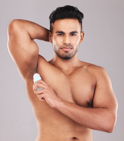 Deodorant, health and man cleaning armpit against a grey studio background. Wellness, care and portrait of a young model with an underarm product for grooming, clean skin and care for body hygieneの写真素材