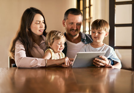 Spending family time online. a young family of four using a digital tablet together at home.の写真素材