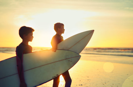 Who needs school when you can surf. two young brothers holding their surfboards while looking...