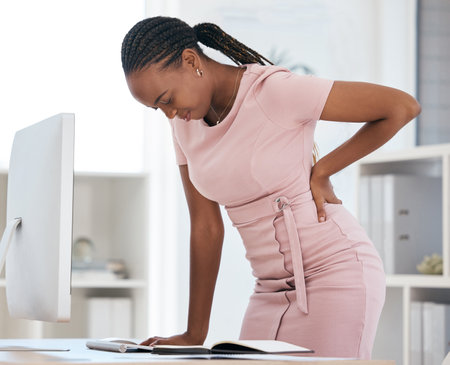 Back pain, bad posture and strain with a black woman in business suffering while working at her desk in the office. Anatomy, spine and cramp with a female employee struggling with backache at workの写真素材