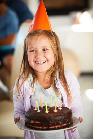 Its not a birthday without a birthday cake. a happy little girl holding a birthday cake with her family in the background.の写真素材