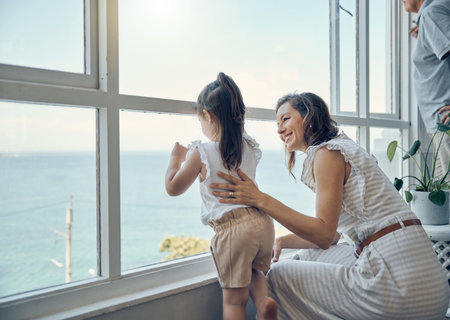 Family view, window and mother with child bonding, having fun and enjoy quality time together in home living room. Mamas love, happiness and mom with kid girl watch the ocean through glass windowの写真素材