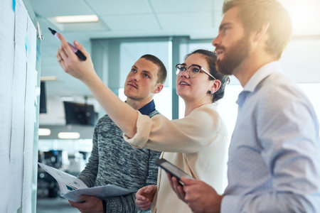 Putting up all their brilliant ideas on the board. a group of businesspeople brainstorming in an...