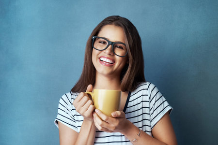 Give me coffee and watch me smile. Studio shot of an attractive young woman having a beverage against a blue background.の写真素材