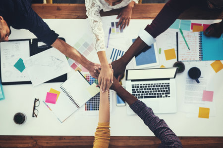 Success belongs to the determined. High angle shot of a group of businesspeople joining their hands in solidarity during a meeting in a modern office.の写真素材