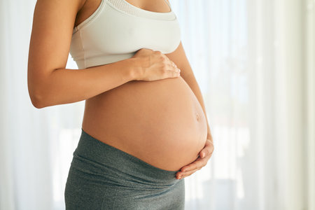 New shape with a purpose. a pregnant woman holding her belly while sitting on her bed.の写真素材