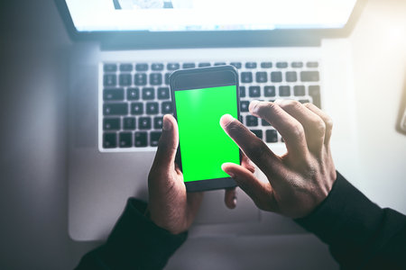 Keeping track of every detail on his wireless devices. High angle shot of an unrecognizable man using a cellphone while working late in the office.の写真素材