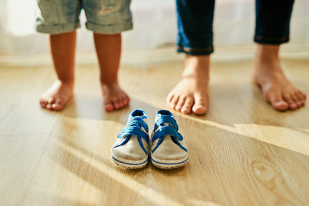Who will fill these little shoes. an unidentifiable mother and her little boys feet standing behind a pair of baby shoes at home.の写真素材
