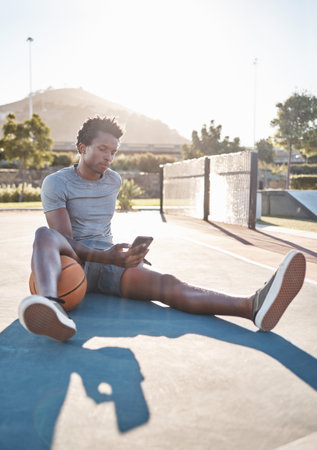 Basketball, phone and man relax on social media, internet and reading news on app outdoor on a court. Black man with 5g smartphone after sport training, exercise and game at sports club in summerの写真素材