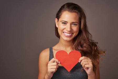 You fill my heart with happiness. Studio shot of an attractive young woman holding a blank red heart against a gray background.の写真素材