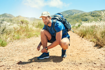 Gearing up for a great hike ahead. a young man tying his shoelaces while out on a hike.の写真素材
