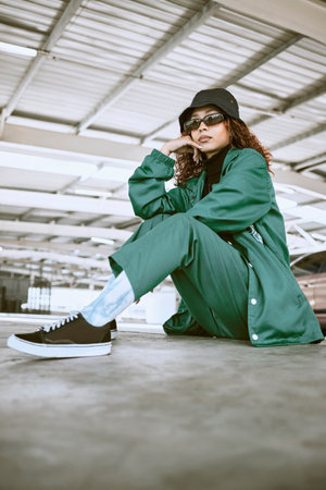 Fashion, style and portrait of woman in parking lot with trendy, stylish and designer clothing. Beauty, freedom and black woman in sitting pose on floor of car park in cool, edgy and urban outfitの写真素材