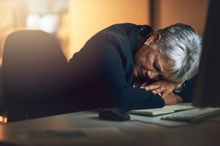 We all have a limit. a mature businesswoman sleeping at her desk during a late night at work.の写真素材