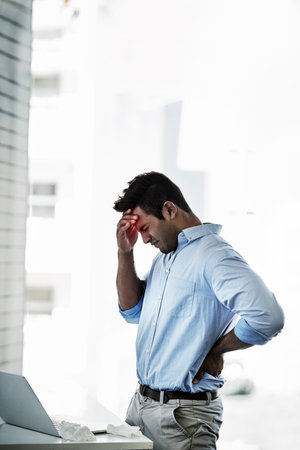 This pain is far too unbearable. a young businessman suffering with a headache and back pain at work.の写真素材