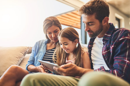 Making quality time an informative one. a mother and father using a digital tablet with their daughter on the sofa at home.の写真素材