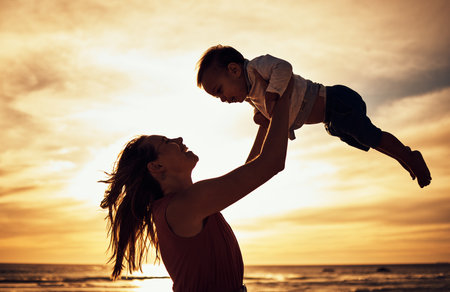 Family, silhouette and beach sunset with mother and baby against golden sky with love, care and support while on vacation in summer. Woman and child happy by sea for travel, adventure and freedomの写真素材