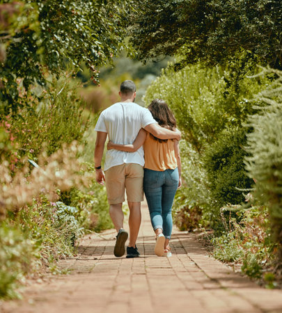 Hug, walk and couple on a path in nature for peace, relax and bonding together in summer. Back of a man and woman with affection, hugging and walking with love in a park or garden during springの写真素材