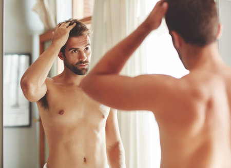 Im having a good hair day. a shirtless young man checking out his hair in the bathroom mirror.の写真素材