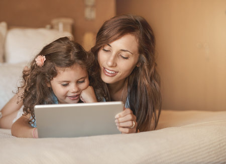 Learning and having fun. a happy mother and daughter having fun at home while playing on a tablet.の写真素材