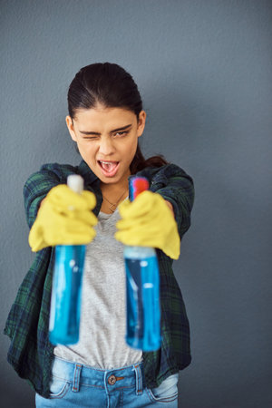 Taking aim at germs. Studio portrait of an attractive young woman taking aim with two spray bottles of disinfectant.の写真素材