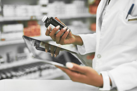 We need more of this kind. a unrecognisable female pharmacist holding a digital tablet in one hand and medication in the other inside of a pharmacy.の写真素材