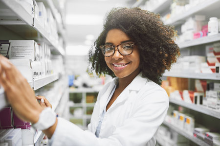 I make sure everything is in its place. Portrait of a cheerful young female pharmacist packing medication on shelves inside of a pharmacy while looking at the camera.の写真素材