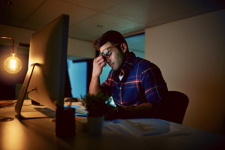 Tonight is just not my night. a young businessman experiencing strain during a late night at work.の写真素材