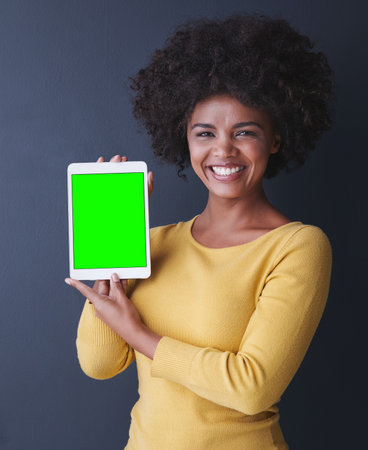 Do you have any idea what your tablet can do. Studio shot of a young woman holding up her tablet against a grey background.の写真素材