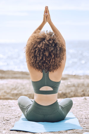 Yoga, zen and back view of black woman at beach on yoga mat outdoors for health, wellness or mobility. Meditation, hands up prayer pose or female training in pilates for exercise, fitness or workout.の写真素材