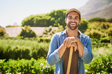 My farm is my life. Portrait of a happy young farmer holding a spade while posing in the fields on his farm.の写真素材