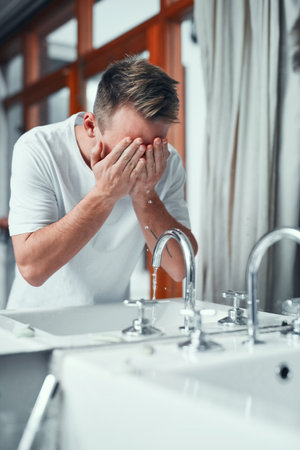 Everyone should follow a good skincare routine. a young man washing his face in the bathroom at home.の写真素材