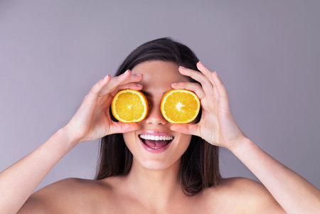 I dont believe my eyes. Studio shot of an attractive young woman holding oranges in front of her eyes against a purple background.の写真素材