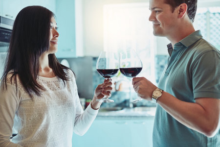 Heres to the best love story. a young couple enjoying a glass of wine at home.の写真素材