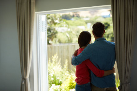 Their happiest place is together. Rear view shot of a mature couple looking out the window at home together.の写真素材