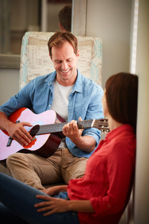 Music is another language of love. a man playing the guitar for his wife at home.