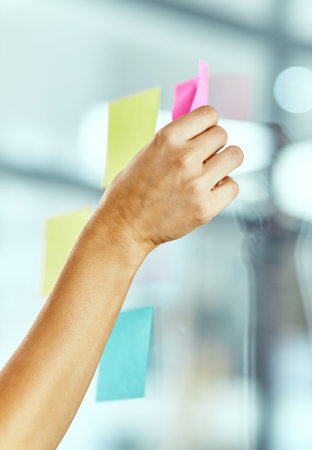 Let the brainstorming begin. a woman pasting notes on glass during a brainstorming session at work.