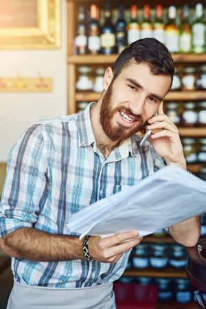 Your business is doing well when youre ordering double. a shop owner talking on his cellphone while looking at paperwork.の写真素材