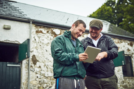 Looks like its a sunny day tomorrow. two cheerful young farmers busy on a digital tablet while...