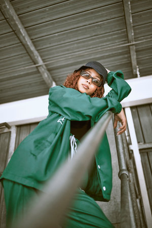 Fashion, street style and woman with green clothes, sunglasses and hat standing on stairs of an urban city building. Portrait of a cool female, hip hop or fashionable hipster model with casual outfitの写真素材