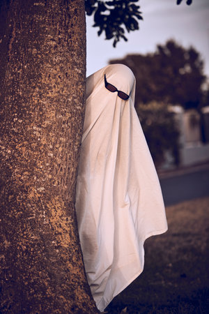 ghost costume, halloween and sunglasses in nature park outdoors. Funny horror dress up, spooky holiday celebration and creative scary mystery spirit design or hiding ghoul with glasses for carnivalの写真素材