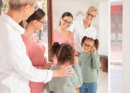 Mirror, glasses and girl with mother and optometrist at optometry shop shopping or trying new spectacles. Smile, vision and happy kid looking at reflection testing eyewear or lenses at optics store.の写真素材