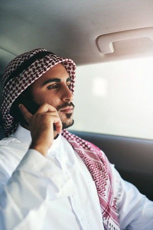Ambition drives him. a young muslim businessman using his phone while traveling in a car.の写真素材
