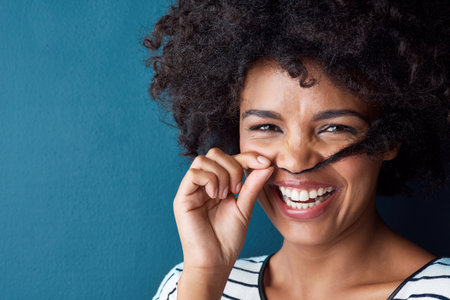 Oh so silly. Studio portrait of an attractive young woman making a moustache with her hair against a blue background.の写真素材