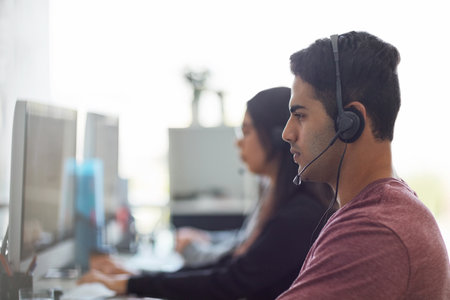 A young man wearing a headset with his colleagues blurred in the background.の写真素材